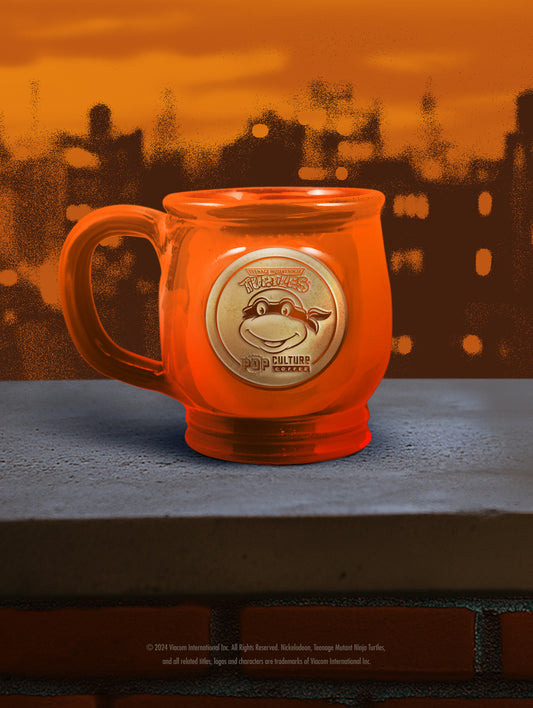 The handthrown stoneware mug for the Teenage Mutant Ninja Turtle, Michelangelo, featuring a vibrant orange glaze.